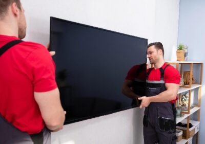 Movers fixing a large flat television on the wall in the living room.
