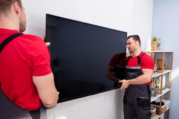 Movers fixing a large flat television on the wall in the living room.